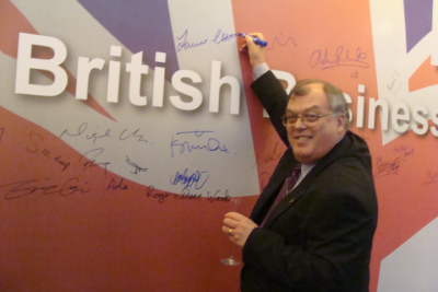 Photo of Laurie Cuthbert signing a Union Jack banner with text reading 'British business'